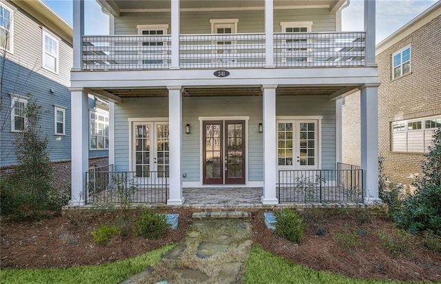 view of exterior entry with a balcony, french doors, and a porch