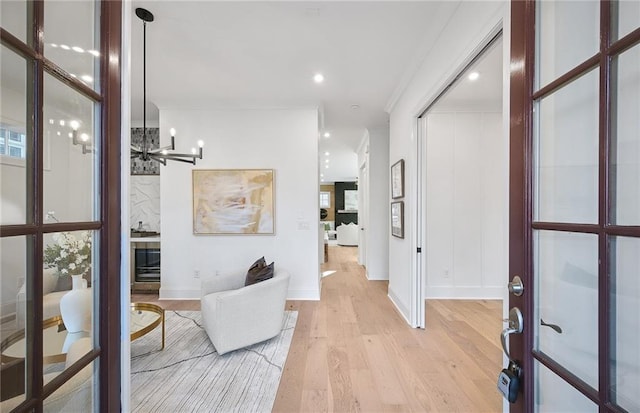 corridor with an inviting chandelier, light wood-type flooring, a wealth of natural light, and crown molding