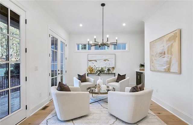 sitting room with french doors, light wood-type flooring, an inviting chandelier, and crown molding