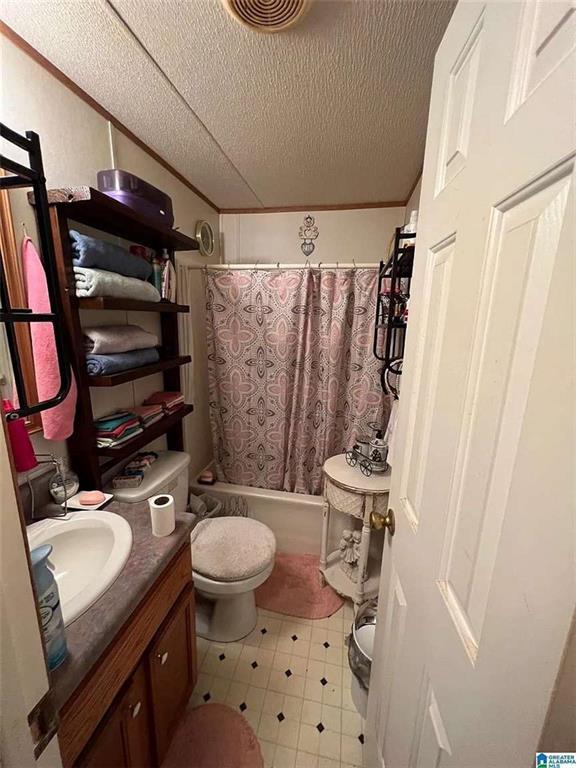 full bathroom with toilet, a textured ceiling, ornamental molding, shower / bath combo with shower curtain, and vanity