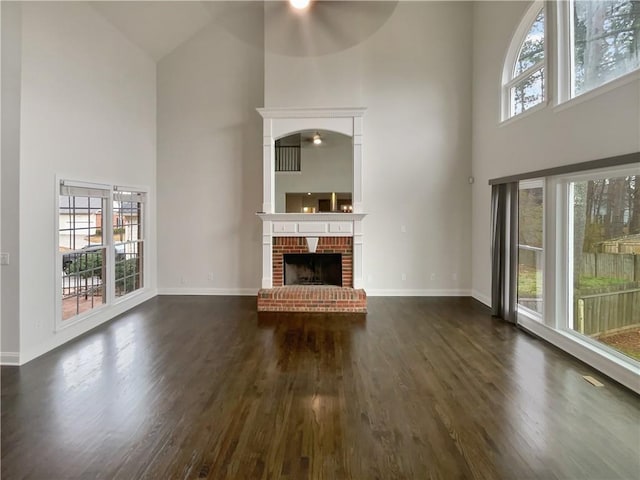 unfurnished living room with dark wood-style floors, baseboards, a fireplace, and a high ceiling