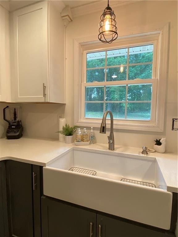 kitchen featuring white cabinets, decorative light fixtures, light countertops, dark cabinetry, and a sink