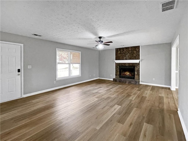 unfurnished living room with hardwood / wood-style floors, a fireplace, a textured ceiling, and ceiling fan