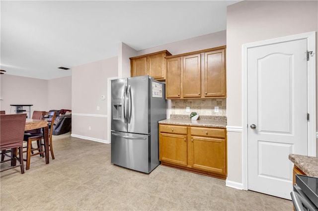 kitchen featuring brown cabinetry, stainless steel refrigerator with ice dispenser, visible vents, tasteful backsplash, and baseboards