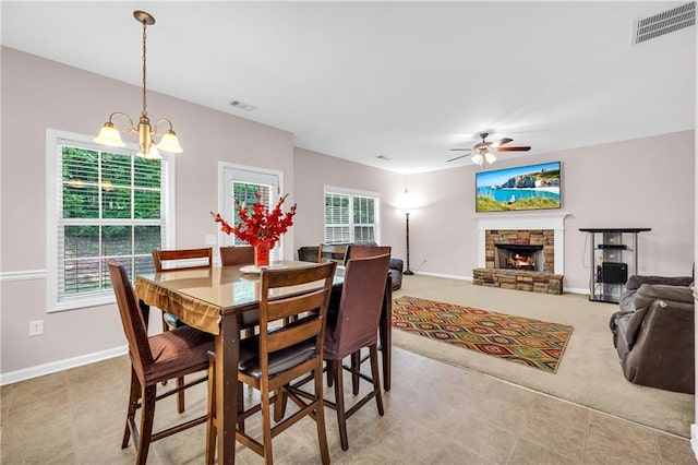 dining room featuring visible vents, baseboards, ceiling fan with notable chandelier, and a stone fireplace