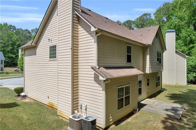 view of home's exterior with a shingled roof, central AC, a chimney, a patio area, and a yard