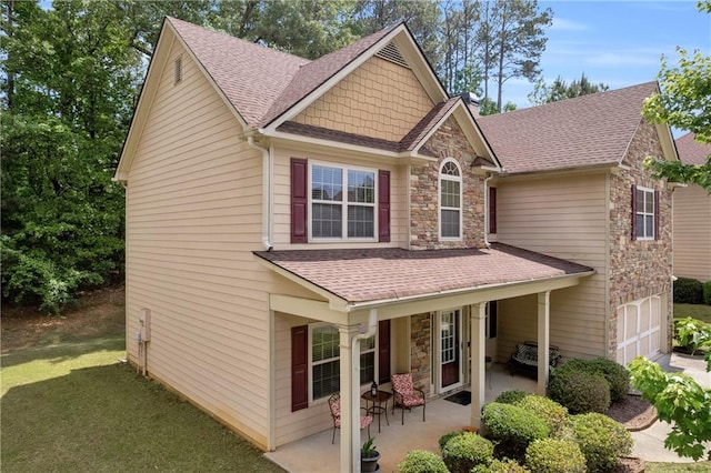 view of front of house featuring a garage, a shingled roof, a front lawn, and stone siding