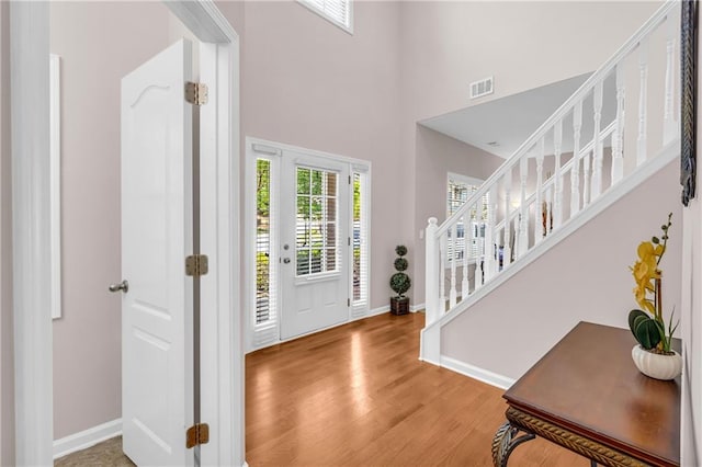 foyer featuring baseboards, wood finished floors, a towering ceiling, visible vents, and stairway