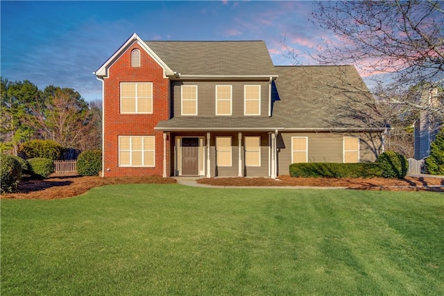 view of front of property featuring brick siding, fence, and a yard