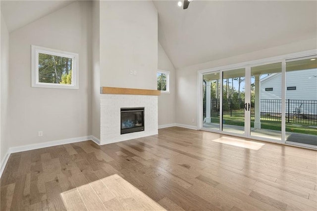 unfurnished living room with high vaulted ceiling, light hardwood / wood-style floors, and a brick fireplace