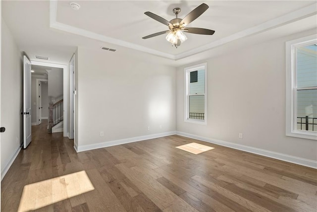 empty room with hardwood / wood-style floors, a tray ceiling, and ceiling fan