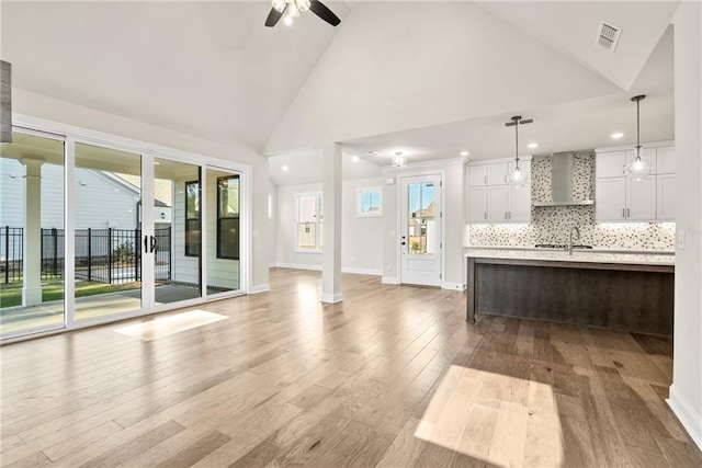 unfurnished living room featuring ceiling fan, light wood-type flooring, sink, and high vaulted ceiling