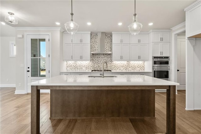 kitchen featuring white cabinetry, pendant lighting, stainless steel double oven, and wall chimney range hood