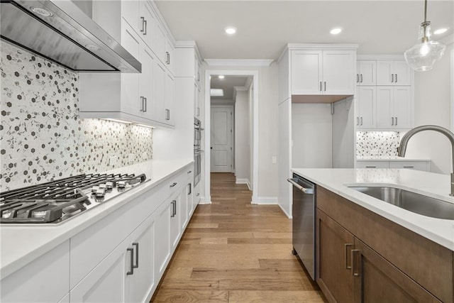 kitchen featuring sink, wall chimney exhaust hood, decorative light fixtures, white cabinets, and appliances with stainless steel finishes