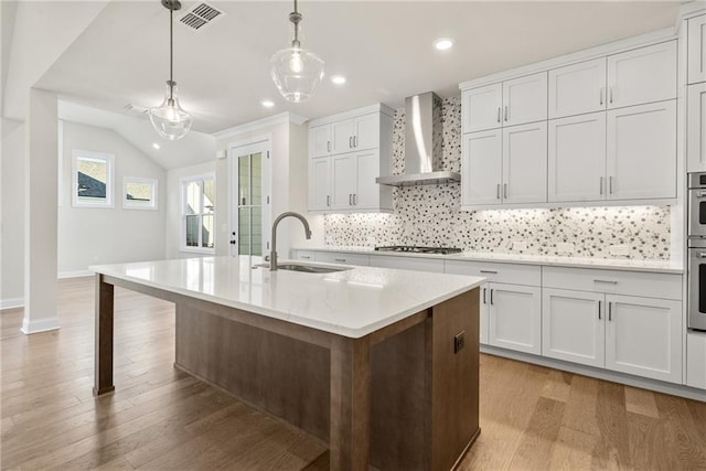 kitchen featuring white cabinetry, sink, wall chimney exhaust hood, and an island with sink