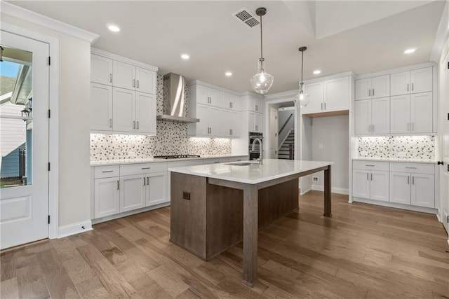 kitchen featuring white cabinets, decorative light fixtures, and wall chimney range hood