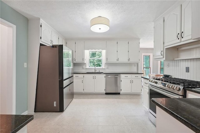 kitchen with sink, light tile patterned floors, a textured ceiling, white cabinetry, and stainless steel appliances