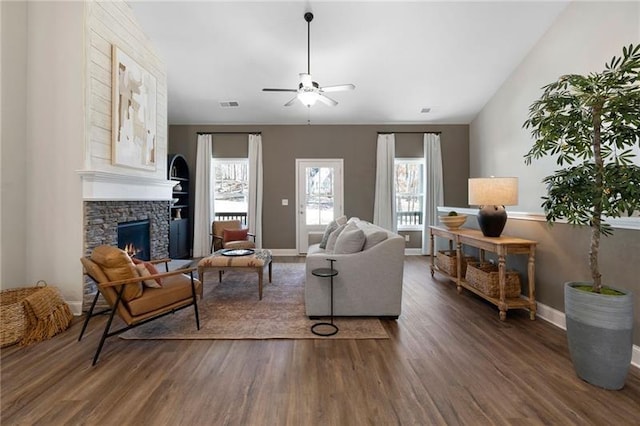 living room with wood finished floors, baseboards, visible vents, a ceiling fan, and a stone fireplace