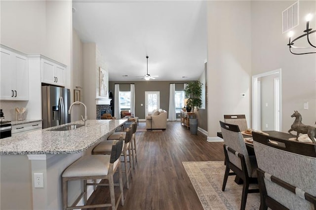 kitchen featuring visible vents, a stone fireplace, stainless steel refrigerator with ice dispenser, white cabinetry, and a sink