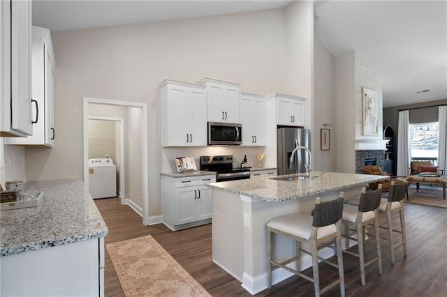 kitchen with washer / dryer, appliances with stainless steel finishes, a fireplace, white cabinetry, and a sink
