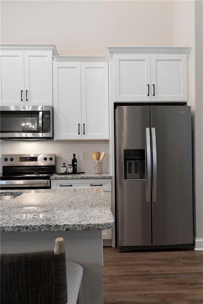 kitchen with backsplash, dark wood finished floors, white cabinetry, appliances with stainless steel finishes, and light stone countertops