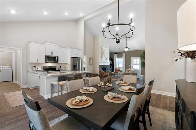 dining room featuring high vaulted ceiling, washer / clothes dryer, dark wood-style floors, a fireplace, and baseboards