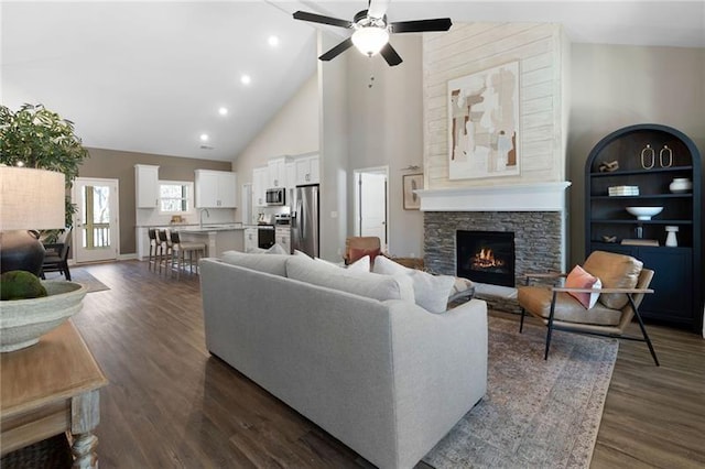 living area with a stone fireplace, high vaulted ceiling, dark wood-type flooring, and a ceiling fan