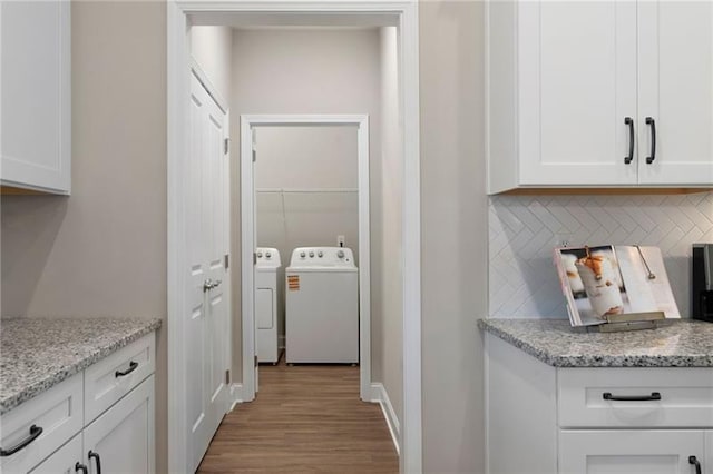 kitchen with independent washer and dryer, backsplash, wood finished floors, white cabinets, and light stone countertops