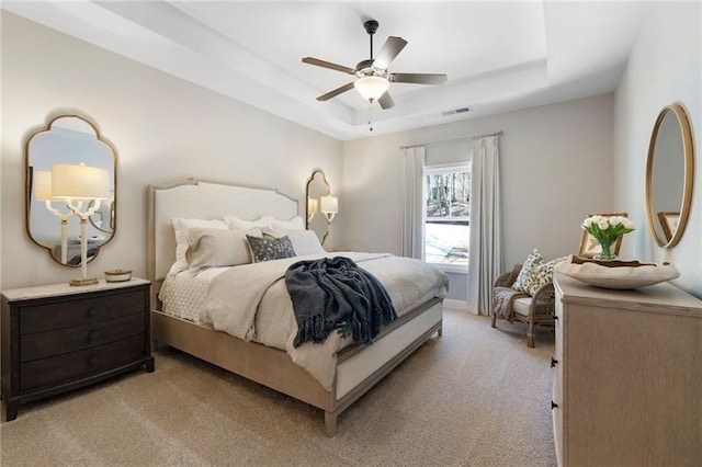 bedroom featuring visible vents, light colored carpet, a tray ceiling, and ceiling fan