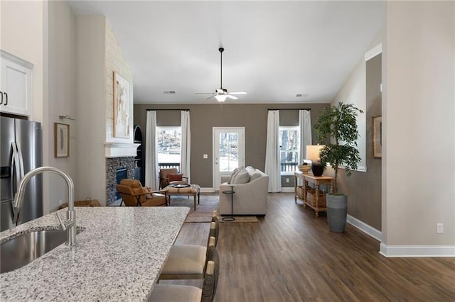 interior space with a ceiling fan, a fireplace, dark wood-style flooring, and baseboards