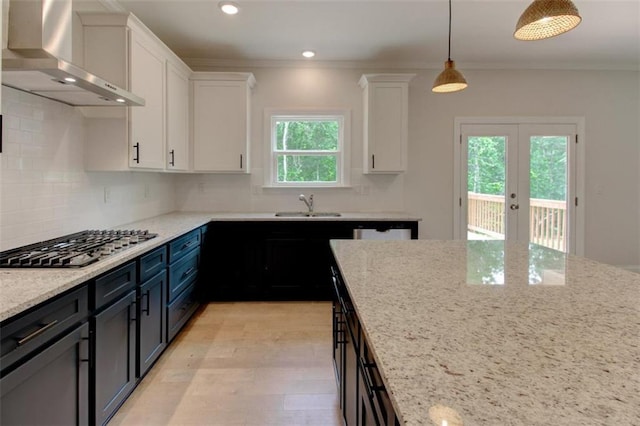 kitchen with stainless steel gas cooktop, a sink, white cabinets, wall chimney range hood, and crown molding