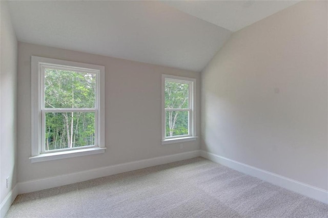 carpeted spare room with a wealth of natural light, vaulted ceiling, and baseboards