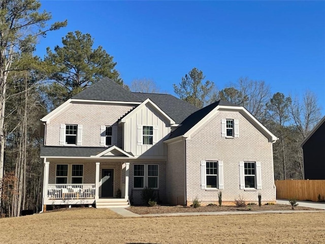 view of front of property featuring covered porch, brick siding, fence, roof with shingles, and board and batten siding