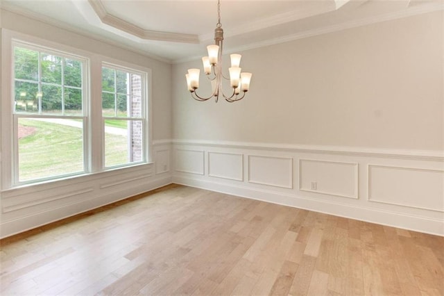 unfurnished room with a decorative wall, a notable chandelier, light wood-type flooring, a raised ceiling, and crown molding