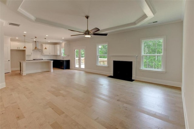 unfurnished living room with light wood-style flooring, a fireplace with flush hearth, visible vents, a raised ceiling, and crown molding