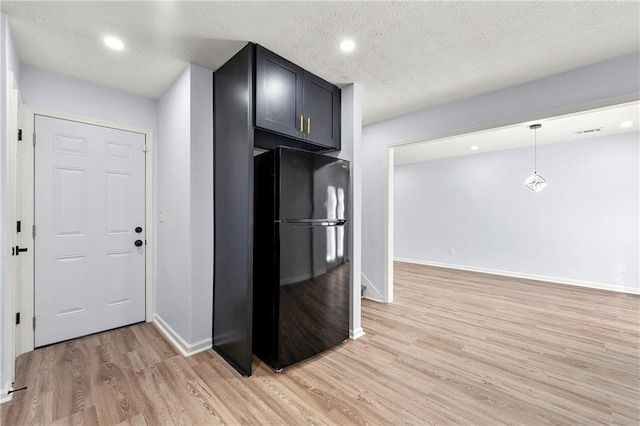 kitchen with black refrigerator, decorative light fixtures, a textured ceiling, and light wood-type flooring