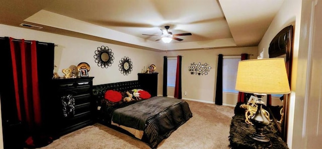 carpeted bedroom with ceiling fan and a tray ceiling