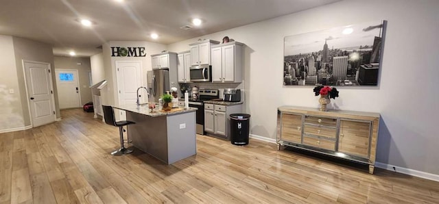 kitchen featuring appliances with stainless steel finishes, a breakfast bar, a kitchen island with sink, and gray cabinetry