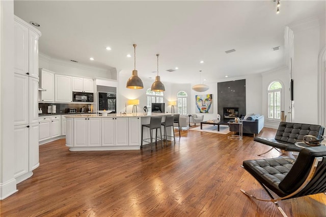 kitchen with hanging light fixtures, white cabinets, black appliances, a center island with sink, and hardwood / wood-style floors