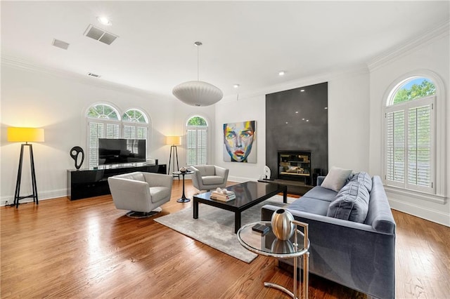 living room with a healthy amount of sunlight, a fireplace, ornamental molding, and hardwood / wood-style flooring