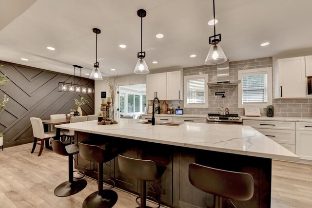 5441 E Main St, Flowery Branch, GA 30542 - kitchen with wall chimney exhaust hood, decorative backsplash, white cabinets, light wood-style floors, and light stone counters