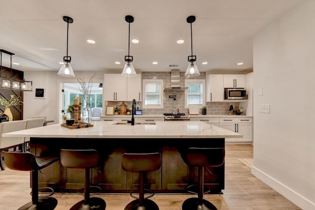 5441 E Main St, Flowery Branch, GA 30542 - kitchen with stainless steel microwave, wall chimney exhaust hood, decorative backsplash, white cabinetry, and light wood finished floors