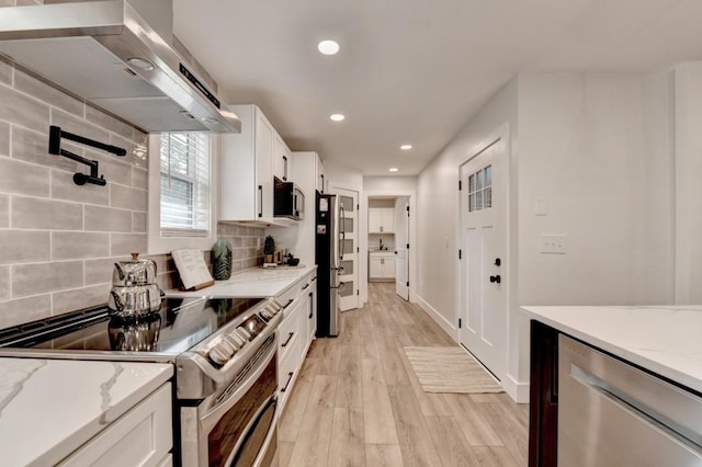 5441 E Main St, Flowery Branch, GA 30542 - kitchen featuring appliances with stainless steel finishes, wall chimney range hood, white cabinets, tasteful backsplash, and light wood finished floors