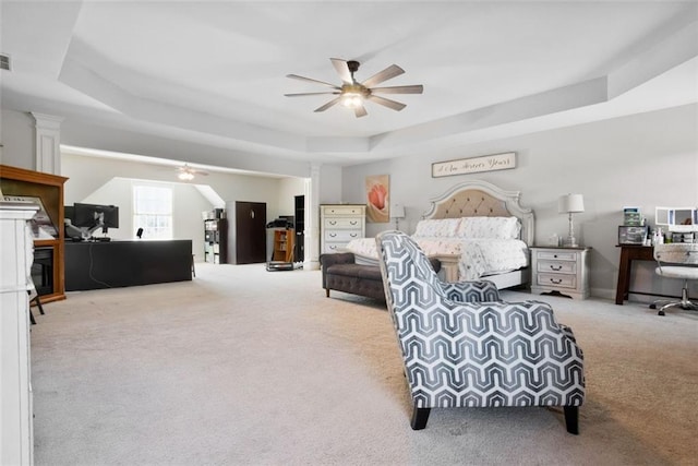 bedroom featuring a raised ceiling, light carpet, and ceiling fan