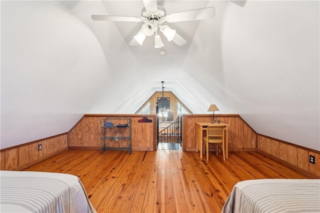 bedroom featuring light wood-style floors, lofted ceiling, a wainscoted wall, and wood walls