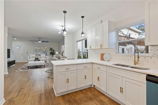 kitchen featuring sink, decorative light fixtures, dishwashing machine, kitchen peninsula, and white cabinets