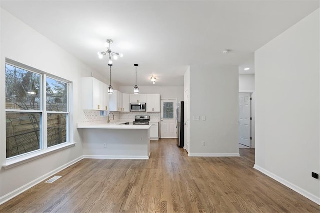 kitchen featuring white cabinetry, decorative light fixtures, appliances with stainless steel finishes, kitchen peninsula, and decorative backsplash