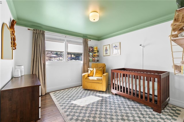 bedroom featuring a crib, wood finished floors, baseboards, and ornamental molding