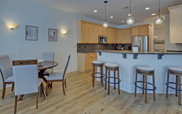 kitchen with light brown cabinetry, hanging light fixtures, and stainless steel appliances