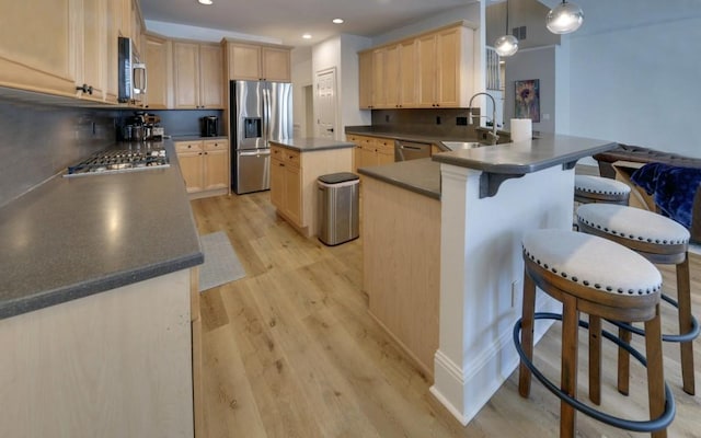 kitchen featuring stainless steel appliances, sink, light brown cabinetry, hanging light fixtures, and a center island